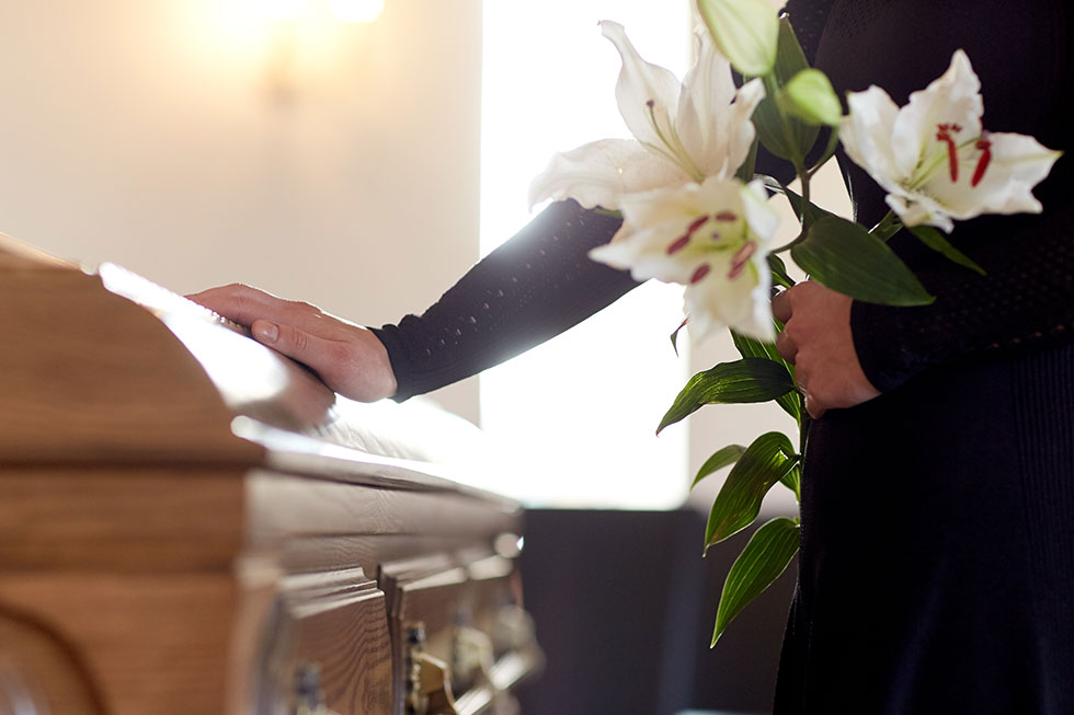 Frau am Sarg Frau mit weißen Blumen nimmt Abschied am Sarg